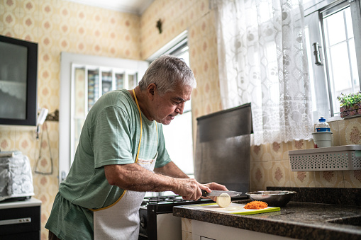 Senior man cutting a onion on the chopping board in kitchen at home