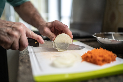 Close-up of a senior man cutting a onion on the cutting board in the kitchen at home