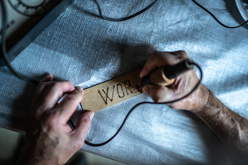 Close-up of a man writing on wood with pyrograph at home