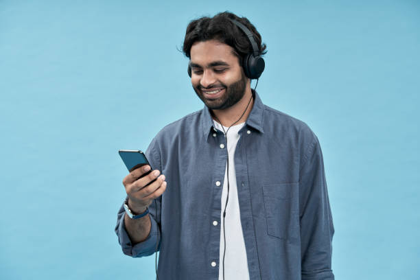 istock Young arab man wearing headphones using mobile phone isolated on blue. 1457443526
