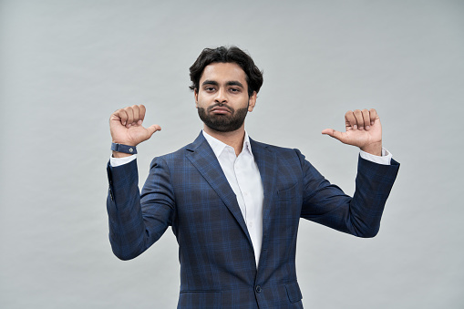Confident proud indian professional business man standing isolated on beige background pointing at himself bragging as choose me concept. Human resources, self-confidence, ego. Portrait.