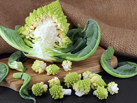 fresh romanesco broccoli, roman cauliflower in florets on wooden cutting board, preparing healthy cabbage vegetables.
