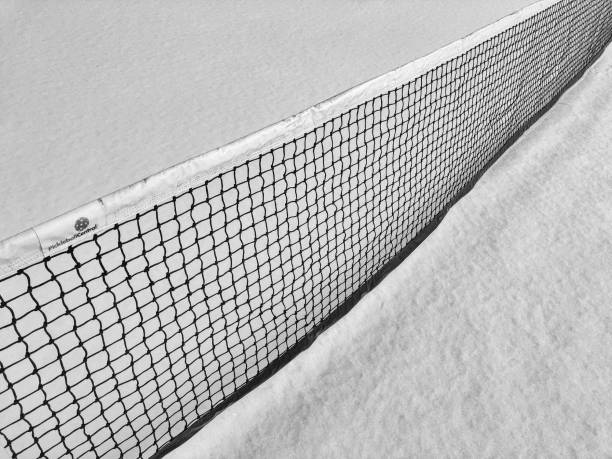 Black and white image of the net on a pickle ball court that is highlighted against fresh snow.