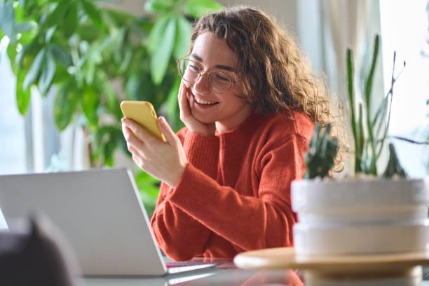 istock Young smiling woman holding smartphone using cellphone sitting at table. 1457447182