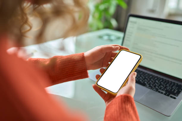 istock Woman holding using mobile phone with mock up screen, over shoulder view. 1457447186