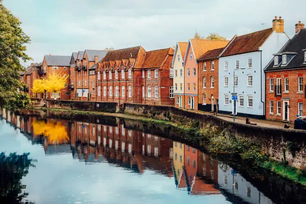 Street view with colorful brick houses near river in the small english town Norwich, England in autumn. Townhouses Buildings At Waterfront. Suburb Houses, Residential Building Near River In Europe