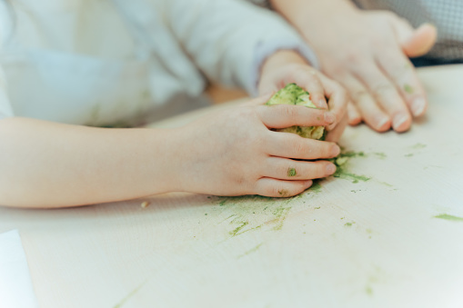 Close up of the hands of young Asian child mixing cookie dough and kneading it on a table while baking or doing bakery.

Moments of young Asian family members, parents and children spending time and having fun together during Christmas winter holidays.
