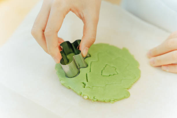 Close up of the hands of young Asian person using the Christmas themed cookie cutter on a green cookie dough on the baking sheet.\n\nMoments of young Asian family members, parents and children spending time and having fun together during Christmas winter holidays.