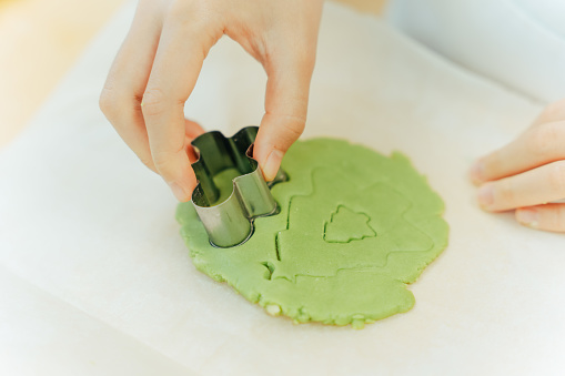 Close up of the hands of young Asian person using the Christmas themed cookie cutter on a green cookie dough on the baking sheet.

Moments of young Asian family members, parents and children spending time and having fun together during Christmas winter holidays.