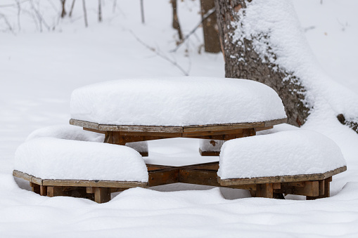 Heavy layer of fresh white snow on picnic table and benches in local public in winter during snowfall. Snow day.