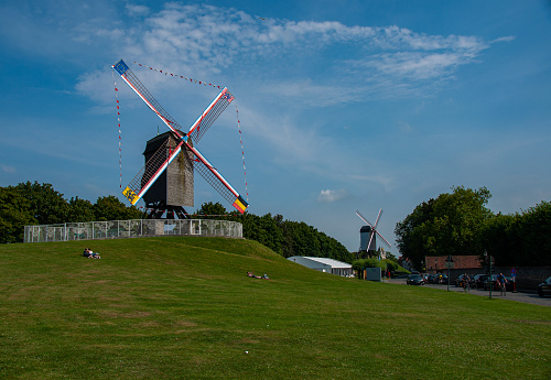 A windmill and a grass field with people on it on a sunny day in Bruges Belgium