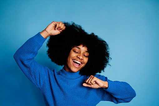 Optimistic African American female with curly hair smiling and looking at camera while standing on blue background