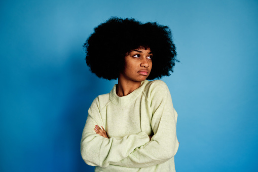 Young African American female with curly hair doing a negation gesture while standing against blue background
