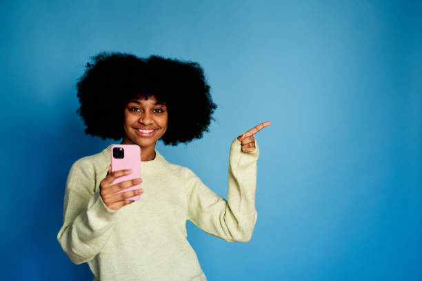 istock Cheerful black woman with smartphone pointing a side 1457468547
