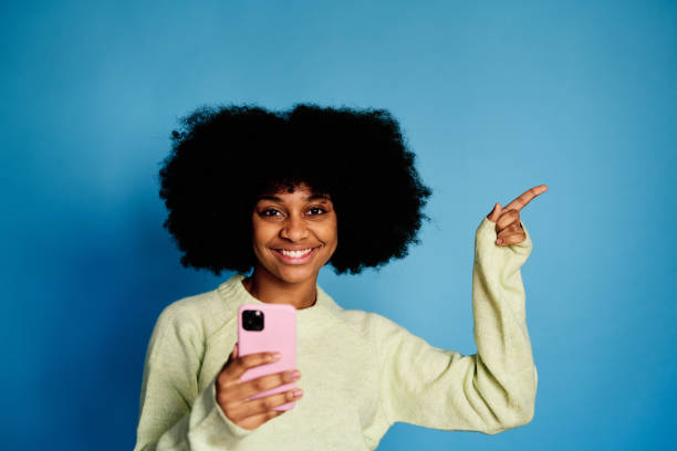 istock Cheerful black woman with smartphone pointing a side 1457468590