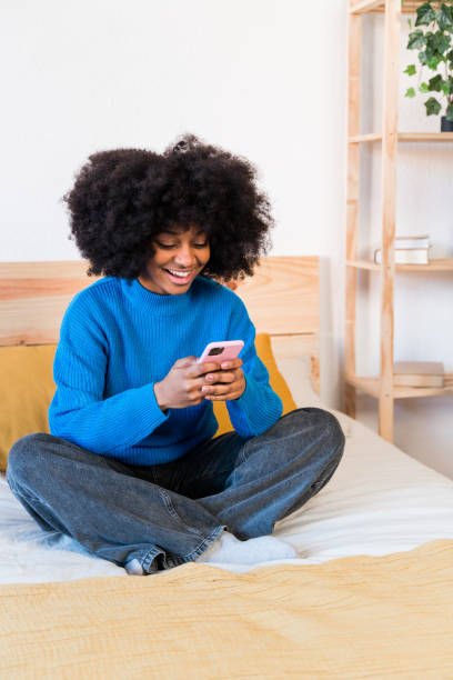 istock Smiling black woman using smartphone on bed 1457474955