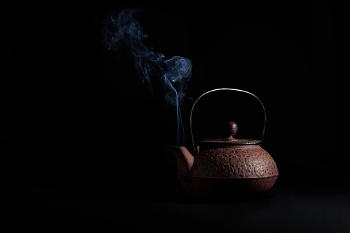 Steaming japanese iron kettle on black background