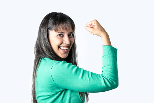 mulher latina real mostrando seus bíceps sobre o fundo branco enquanto olha para a câmera. direitos das mulheres e conceito de empoderamento - satisfaction clothing argentina smiling - fotografias e filmes do acervo