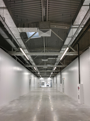 Perspective view of an empty hangar hall under construction with communications on the ceiling. Industrial lighted warehouse.