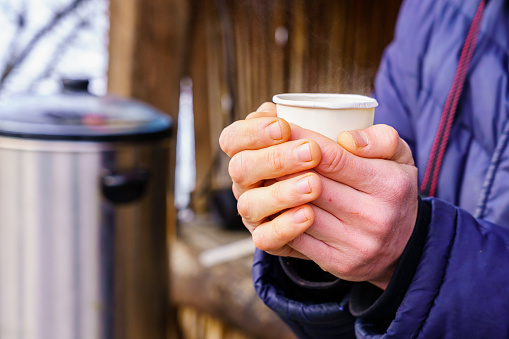 Frozen hands hold a disposable paper cup with hot tea. Warming in cold winter. Selective focus. Background with copy space for text