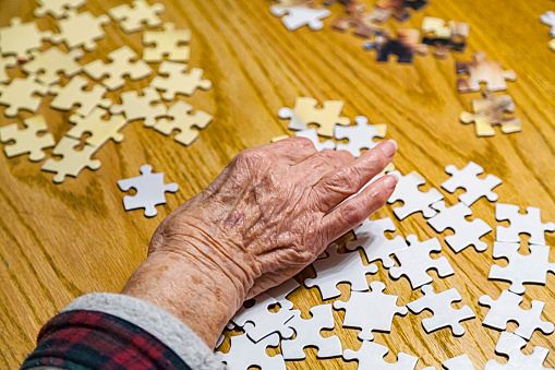 Elderly senior adult woman's hand reaching for jigsaw pieces to assemble a jigsaw puzzle.\n\nNOTE: These are random jigsaw pieces mixed together for the photo shoot from several generic jigsaw puzzles.