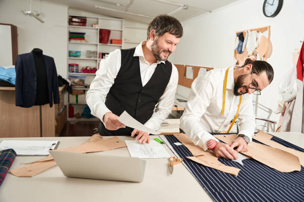istock Young tailor working in atelier monitored by his coworker 1457490980