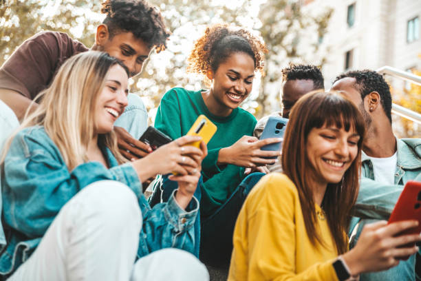 istock Group of multiracial young people using smart mobile phone device outdoors - Happy university students watching cellphones sitting in college campus - Teenagers addicted to social media technology 1457491223