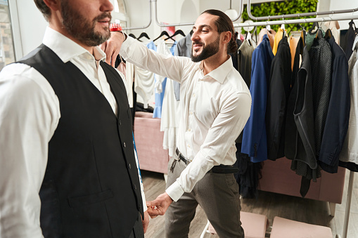 Smiling tailor measuring customer sleeve length in his fashion design studio