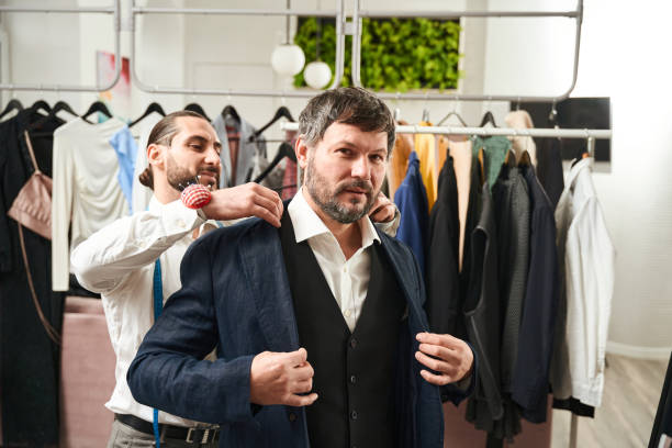 istock Man putting on jacket in presence of clothier 1457491842