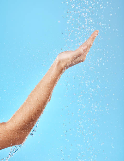 Hand, shower and water for skincare hygiene, wash or dermatology against a blue studio background. Arm and hands of person in healthy wellness, skin hydration and washing for body care treatment manos, ducha y agua para la higiene del cuidado de la piel, el lavado o la dermatología sobre un fondo de estudio azul. brazo y manos de la persona en bienestar saludable, hidratación de la piel y lavado para el tratamiento del cuidado del cuerpo