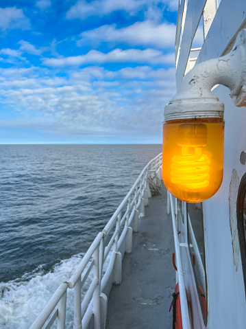 Bright orange / amber nautical style light hanging on the side of a white ferry boat. Views from the deck of the boat looking out to the horizon and deep land moody lake waters. Located in the Upper Peninsula of Michigan between Copper Harbor and Isle Royale.