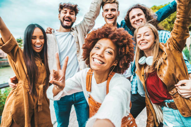 Happy multiracial friends taking selfie picture outside - Group of young people smiling together at camera outdoors - Teenagers having fun walking on city street - Youth culture and friendship concept stock photo