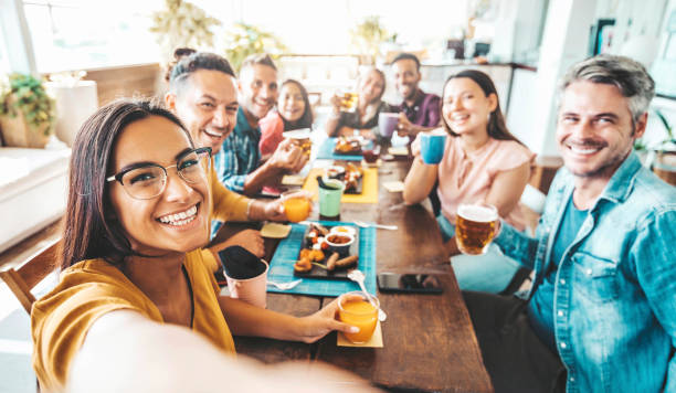 gruppo multirazziale di amici che cenano seduti al tavolino del bar - i giovani si godono il pasto all'ora del brunch mattutino - concetto di stile di vita con donne e uomini al bar del caffè della pausa pranzo - dining table people foods and drinks restaurant foto e immagini stock