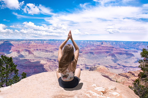 Carefree woman sitting on top of the mountain  meditating. South Rim, Grand Canyon National Park, Arizona, USA.
