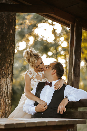 Romantic wedding couple sitting on bench in wooden gazebo in nature