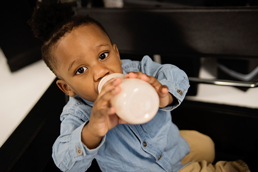 Portrait of adorable black little boy drinking milk in bottle. He is 18 months and is looking at the camera. Horizontal head and shoulder indoors shot with copy space. This was taken in Montreal, Quebec, Canada.