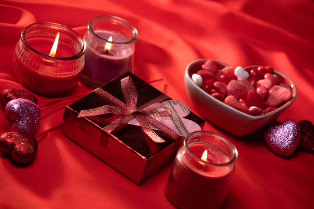 Gift box with a bow and alight candle on pink background
