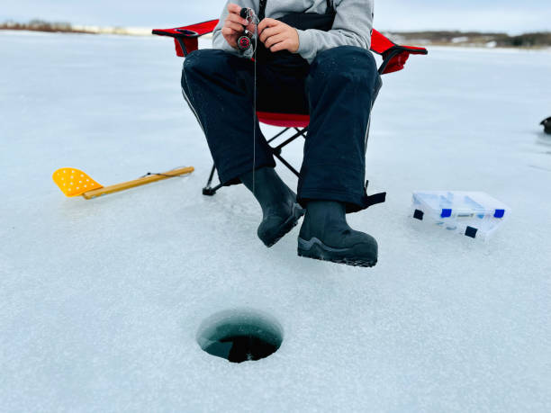 Young man Ice fishing Young man sitting in a chair ice fishing in Alberta. canada flag blue sky clouds stock pictures, royalty-free photos & images