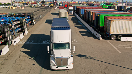 Aerial view of a line of trucks driving through a container yard in the Port of Los Angeles. \n\nAuthorization was obtained from the Los Angeles Harbor Department and Los Angeles Port Police for this operation in restricted airspace.