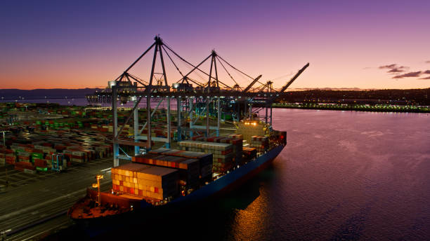 Aerial View Over Channel Towards Docked Container Ship in Port of LA at Twilight Aerial shot of a massive ship in the Port of Los Angeles at twilight, and the vast intermodal container terminal on the dockside. 

Authorization was obtained from the Los Angeles Harbor Department and Los Angeles Port Police for this operation in restricted airspace. san pedro los angeles photos stock pictures, royalty-free photos & images