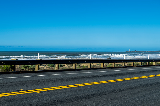California High 1 road running alongside a view of the waves breaking in the Pacific Ocean and a lighthouse in the far distance.

Taken on the Central California Coast.