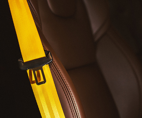 Automobile leather seat of a modern luxury car with a yellow safety belt. Yellow seat belt in a sports car close-up, blurry background. Brown leather car seat. Fasten your seat belts.