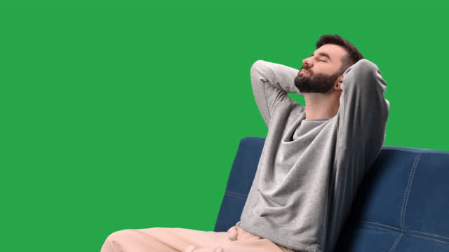 Relaxed man stress free sitting on couch with hands behind head closed eyes chroma key green screen