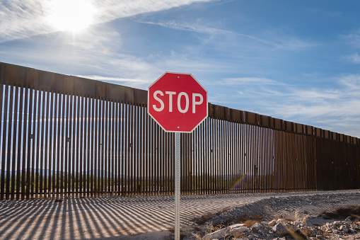 New border wall at US - Mexico border in Arizona with bright red stop sign in foreground intended as a warning to keep undocumented or illegal immigrants out of the United States