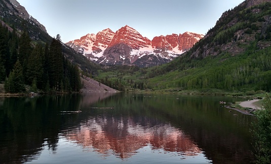 Maroon Bells near Aspen Colorado at sunrise. The sun enhances the vibrant red color in the rock as it gets higher in the sky. A popular photo opportunity for photographers.