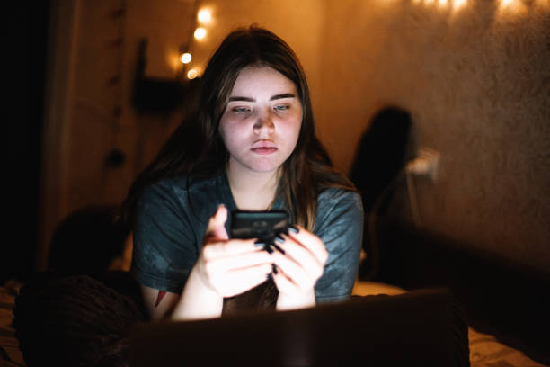 istock Young female teenage student using smart phone and laptop computer while sitting in bed at home at night 1457538566
