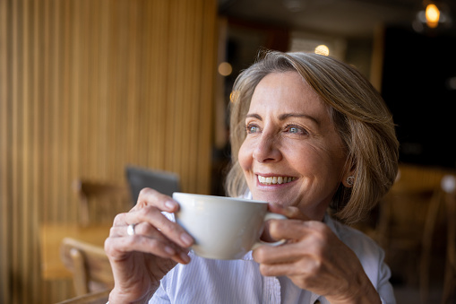 Happy Latin American senior woman drinking a cup of coffee at a cafe and smiling - lifestyle concepts