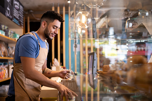 Waiter working at a cafe preparing a delivery order behind the counter - food service occupation concepts