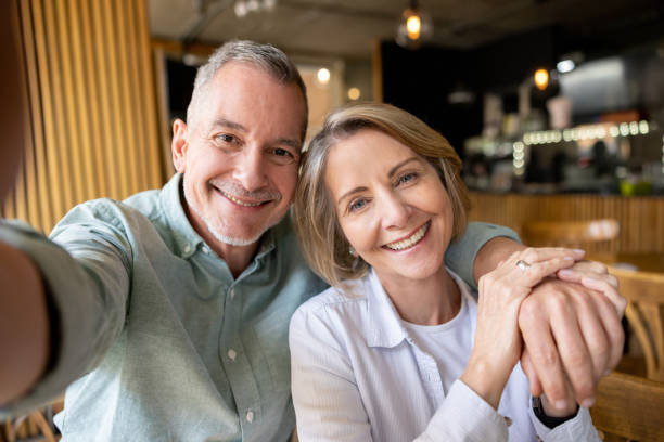 senior couple taking a selfie at a cafe and smiling at the camera - latin american and hispanic ethnicity senior adult mature adult couple imagens e fotografias de stock