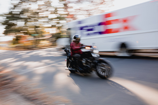 Person ride a motorcycle with a fed ex delivery truck in the background. Panning effect for motion blur.